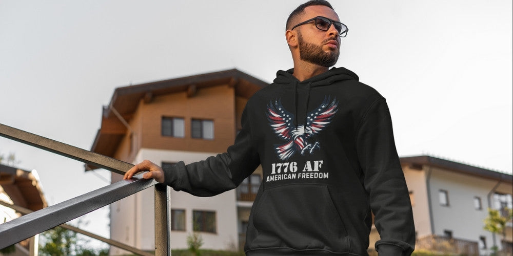 Man wearing a 1776 AF American Freedom black hoodie with a vintage grunge red, white and blue bald eagle design and text, standing outdoors, by Infidel Collective.