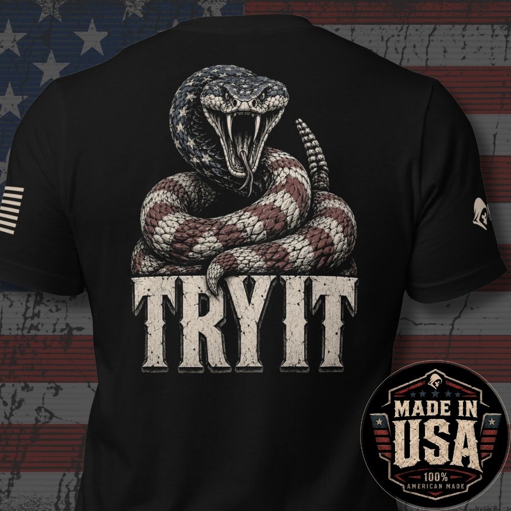 Black short-sleeve t-shirt shown from the back with a large graphic of a coiled snake above distressed white text reading 'TRY IT'. The shirt is photographed against a rustic American flag background, with a circular 'Made in USA 100% American Made' badge overlaid in the lower right corner.