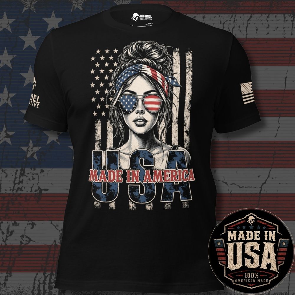 A black short-sleeve graphic T-shirt displayed against a distressed American flag background. The shirt features a central illustration of a woman with an American flag bandana, sunglasses, and the text 'USA' and 'MADE IN AMERICA' in red, white, and blue.