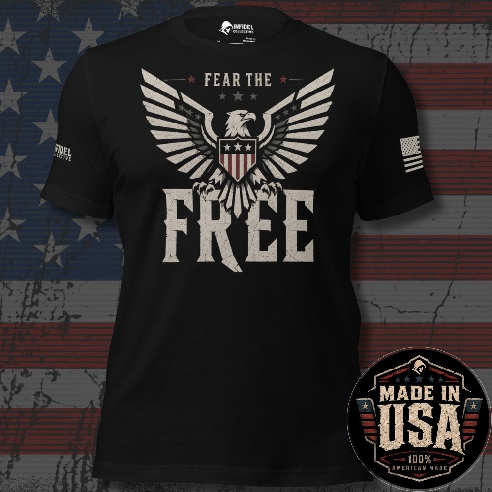 A black short-sleeve graphic T-shirt displayed against a distressed American flag background. The shirt features a large eagle graphic with outstretched wings and the words 'FEAR THE FREE' in distressed white and gray lettering. A round emblem indicates this design is 100% American Made - Made in the USA.