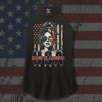 A black raglan sleeveless tank top featuring a patriotic graphic of a woman with an American flag headband and sunglasses, with the text 'MADE IN AMERICA' and 'USA' printed below, displayed against a distressed American flag background.