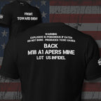 Claymore inspired design with "FRONT TOWARD ENEMY" across the front and "M18 A1 APERS MINE LOT IS-INFIDEL" across the black on a black tee against a USA flag background.