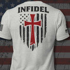 A light heather gray t-shirt shown from the back, featuring a large graphic print with the word 'INFIDEL' in black above a distressed American flag design with a prominent red cross.
