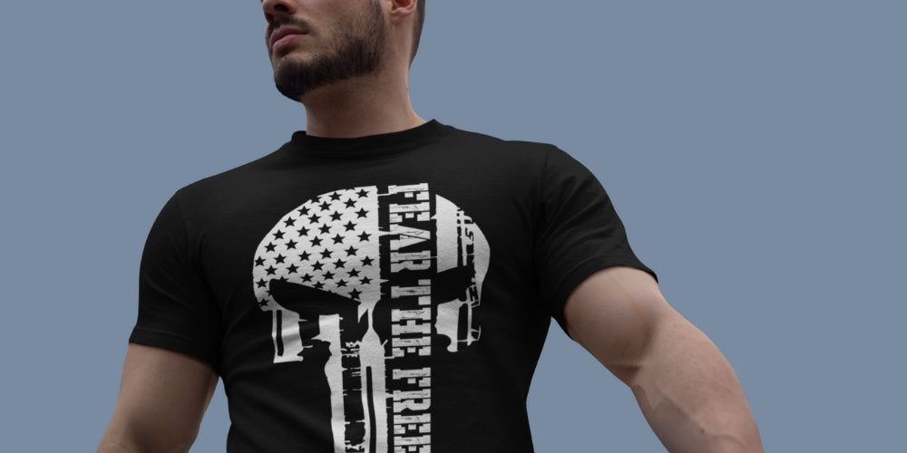 Man wearing a black t-shirt with a white graphic design of Punisher skull representing monochrome USA flag with text running vertically "Fear the Free", by Infidel Collective.