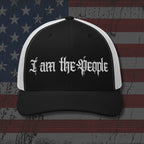 Black and white cap with 'I am the people' text on an American flag background