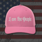 Pink cap with 'I am the people' text on an American flag background