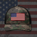 Camouflage cap with American flag patch on a background resembling the American flag.
