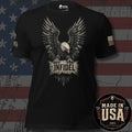 Bronze bald eagle with plaque stating "INFIDEL" across the chest of a black tee with a USA flag on the left sleeve and brand logo "INFIDEL COLLECTIVE" on the right sleeve, against a distressed USA Flag background and a badge stating "MADE IN THE USA".