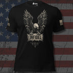 A black short-sleeve graphic t-shirt featuring a large distressed eagle design with the word 'INFIDEL' on the chest, displayed against a rustic American flag background.