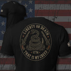 Black tee with back print featuring a coiled rattlesnake, crossed flintlock pistols, 1776, and the text Liberty or Death That Is My Creed