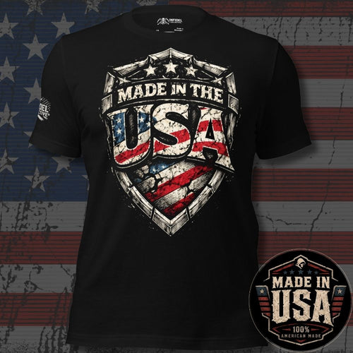 A black short-sleeve graphic T-shirt displayed against a distressed American flag background. The shirt features a large shield-style chest graphic reading "MADE IN THE USA" with an American flag pattern inside the letters.
