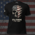 Black t-shirt with skull and American flag design with text 'STILL STANDING 1776 / 2026' on a distressed American flag background