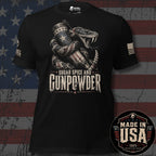 A black short-sleeve graphic T-shirt displayed against a distressed American flag background. The shirt features a large front print of a coiled snake wrapped around a patriotic American flag cylinder, with the text 'SUGAR SPICE AND GUNPOWDER' below. Brand logo INFIDEL COLLECTIVE on right sleeve and USA American flag on left. Made In The USA badge in lower right corner.