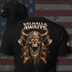 Black ghosted mockup with Viking skull and axes graphic and 'VALHALLA AWAITS' across the back of the tee, with a USA flag backdrop.