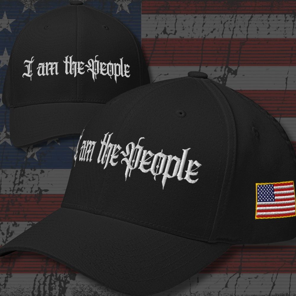 Two black baseball caps with 'I am the People' embroidered in white Gothic lettering, shown against a distressed American flag background. One cap features a small embroidered US flag patch on the side.