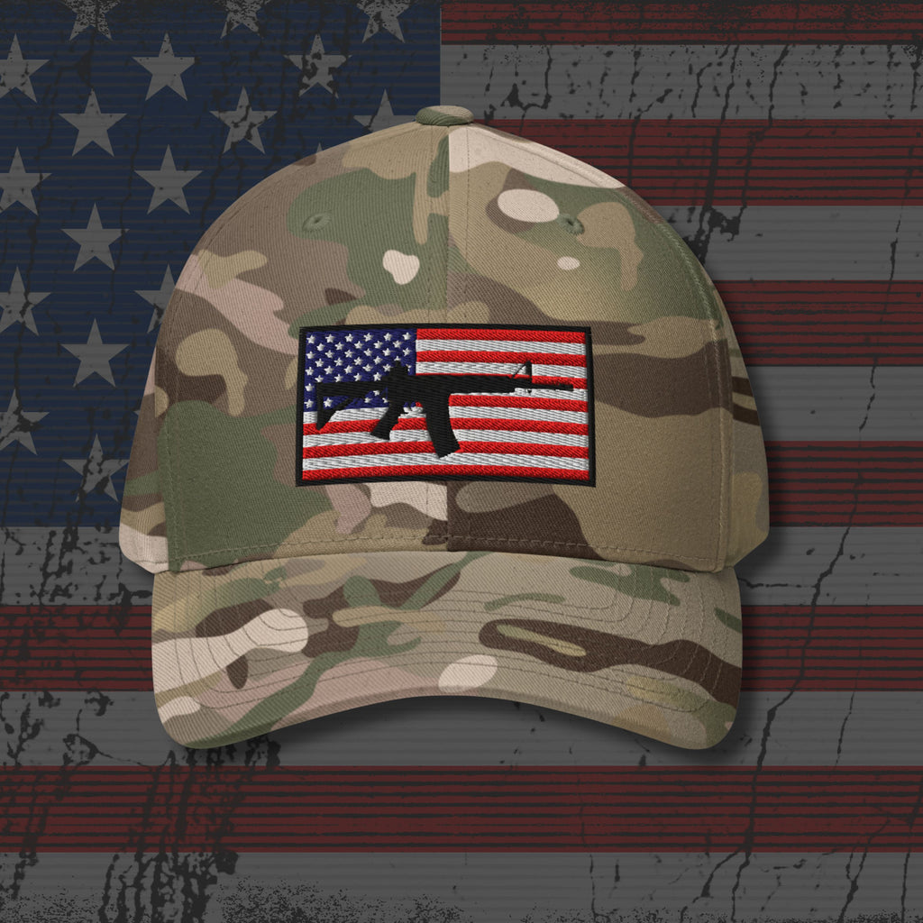 Camouflage baseball cap with an American flag patch featuring a rifle on a textured American flag background.
