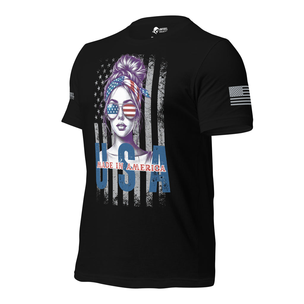 A black short-sleeve t-shirt with a patriotic graphic on the front featuring a stylized woman's face with an American flag headband and sunglasses, a distressed American flag background, and 'MADE IN AMERICA' text. A small American flag is printed on the left sleeve.